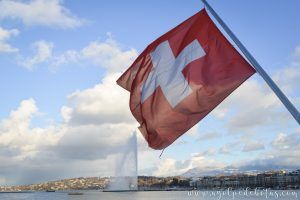 Bandera de Suiza en primer plano con el Jet d'Eau de fondo. Uno de los puntos más emblemáticos de la ciudad de Ginebra