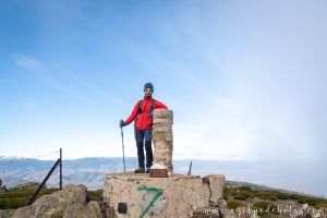 Montañero junto al hito de piedra en el punto más alto del pico Mondalino en Bustarviejo