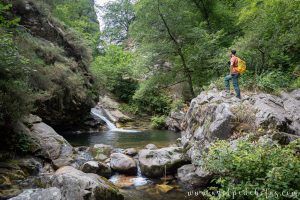 Hombre posando en una piedra junto a uno de los saltos de agua de la ruta de senderismo de la Ruta del Alba en el parque natural de Redes en Asturias
