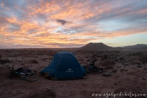 Tienda de campaña y bicicletas en un desierto al amanecer