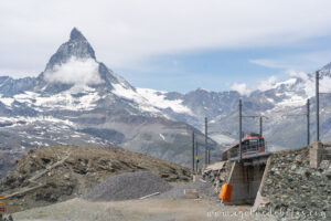 Estación de Gornergrat con el tren cremallera y montañas nevadas al fondo en un día nublado.