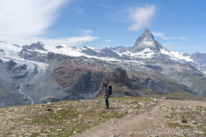Hombre caminando por un sendero con los Alpes suizos de fondo, y la montaña Matterhorn como gran protagonista