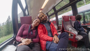Pareja viajando en el tren panorámico entre Täsch y Zermatt, disfrutando del paisaje alpino durante su viaje por Suiza con niños
